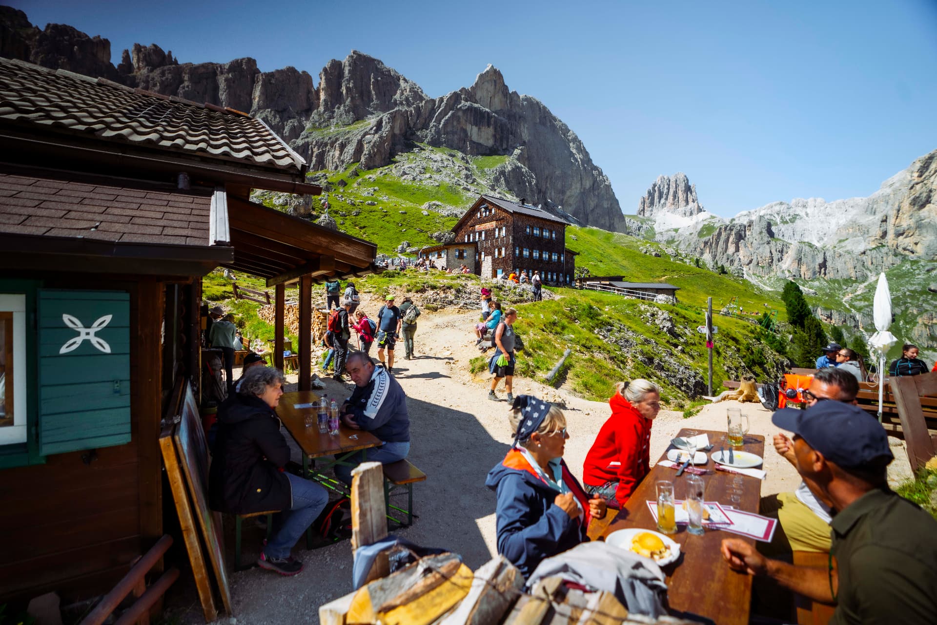 Wanderer an Holztischen vor einer Berghütte in den Dolomiten