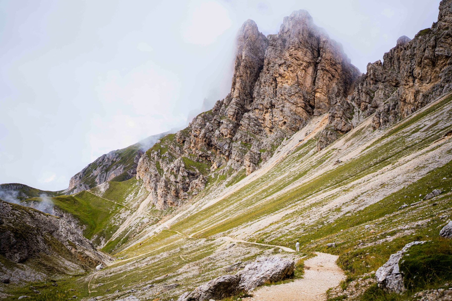 Bergpfad unter zerklüfteten Gipfeln in ziehenden Wolken